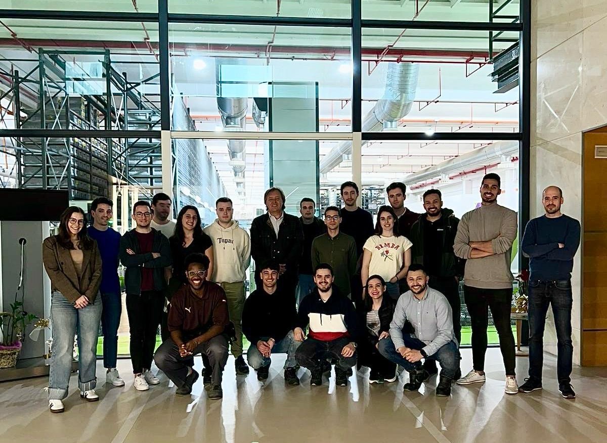 Fotografía de los estudiantes del Máster en Operaciones Productivas y Logísticas de la Universidad de Zaragoza en el área de acceso al centro logístico de Novaltia, con la zona automatizada del almacén visible al fondo.